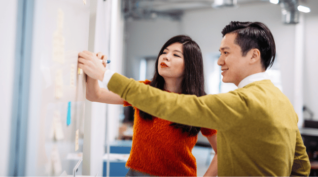 Two people standing in front of a whiteboard.