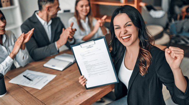 A female professional is holding up a piece of paper in front of a group.